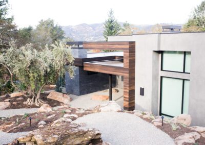 Modern house with wooden accents surrounded by a landscaped garden with rocks and native plants.